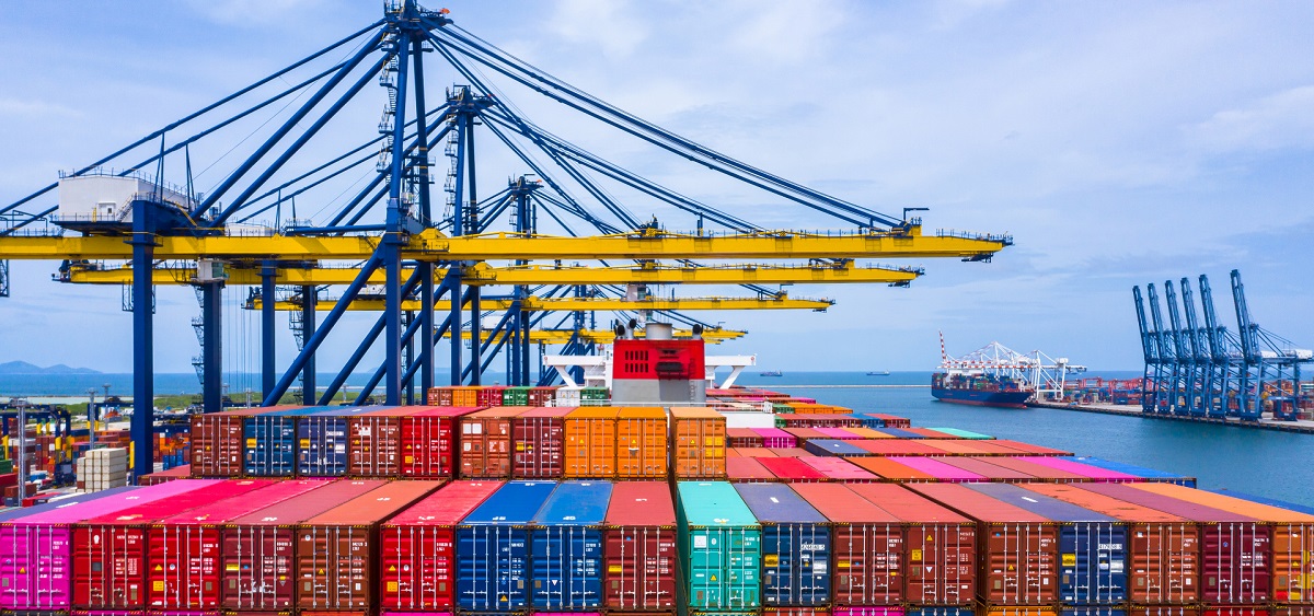 Aerial view of a cargo ship docked at a port, being loaded with colorful shipping containers by cranes.