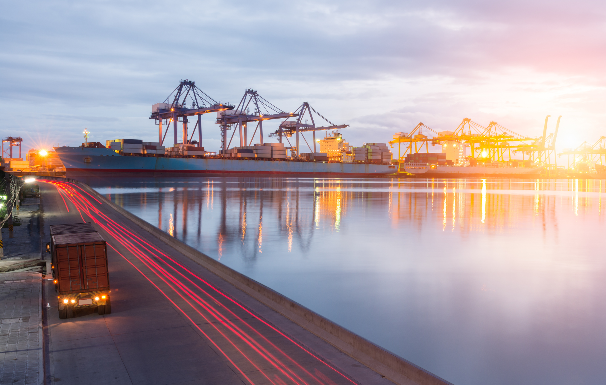 Long exposure photograph of a bustling port with trucks, ships, and logistics operations.